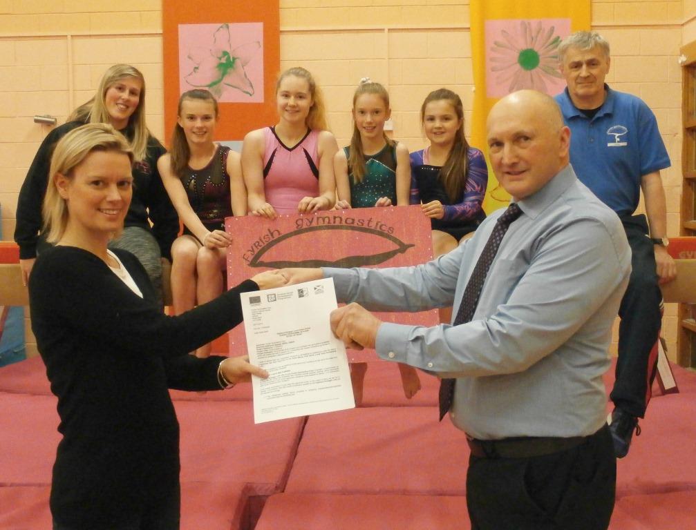 Tom Davis, Chair of the Inner Moray Firth North LEADER Local Area Partnership, presents award to Claire Bath, Chair of Fryish Gymnastics Club with Senior Coach Sonny Rhind and some of the young gymnasts looking on.